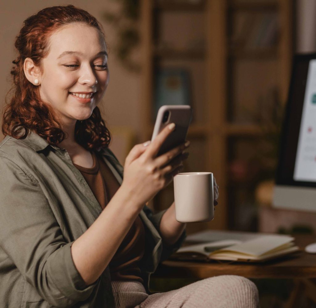 mujer-casa-smartphone-frente-computadora-mientras-toma-cafe